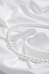 Photo of Beautiful pearls on white silk, closeup view