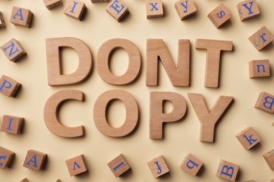 Photo of Words Don't Copy made of wooden letters and cubes on beige background, flat lay. Plagiarism concept