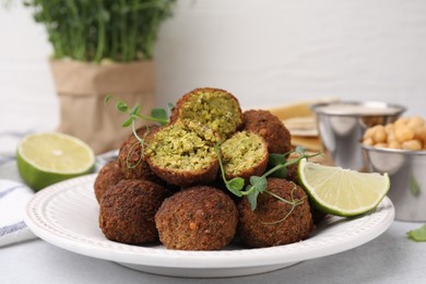 Photo of Delicious falafel balls, lime and microgreens on light table