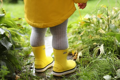 Photo of Little girl wearing rubber boots standing in puddle outdoors, closeup. Back view