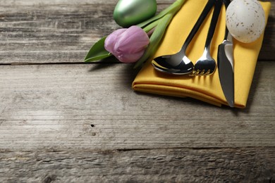 Photo of Cutlery set, painted eggs and beautiful flower on wooden table, closeup with space for text. Easter celebration