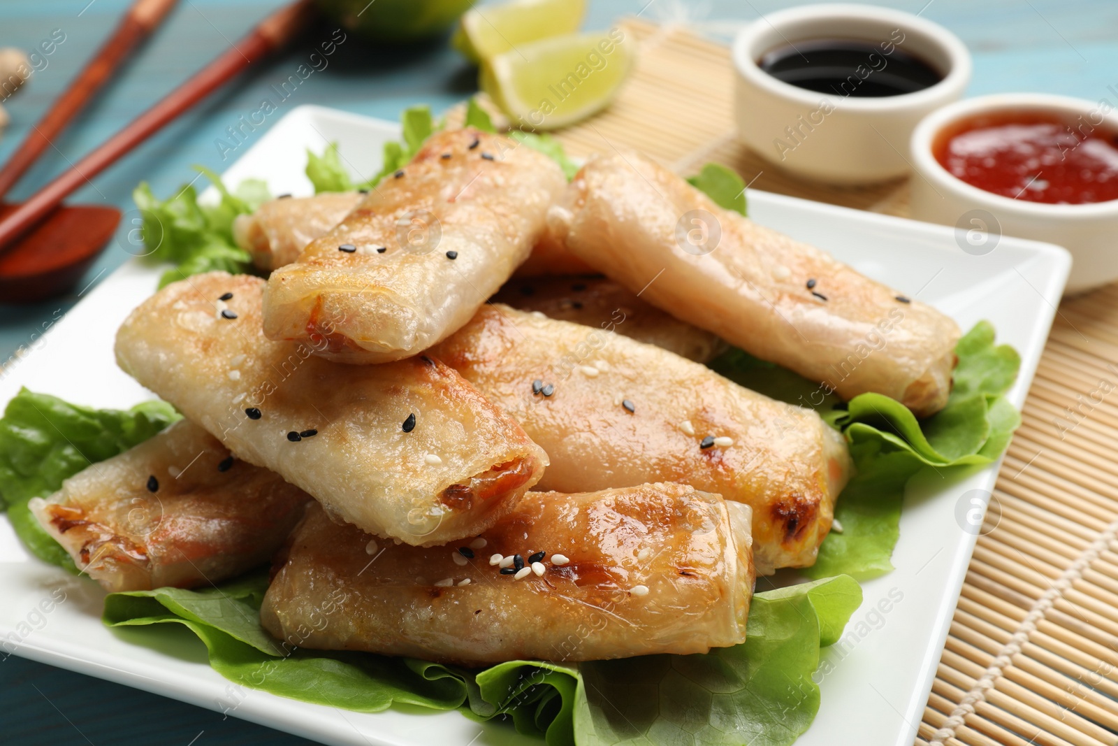 Photo of Tasty fried spring rolls and lettuce on light blue wooden table, closeup