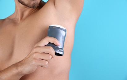 Photo of Young man using deodorant on color background, closeup. Space for text