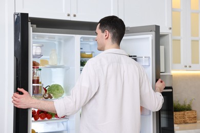 Photo of Happy man near refrigerator in kitchen at home, back view