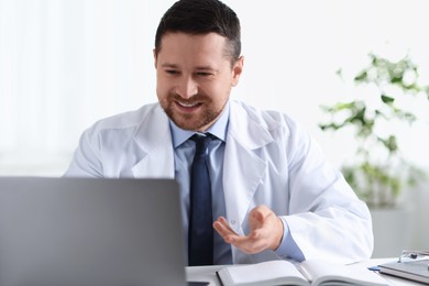 Smiling doctor having online consultation via laptop at table in clinic