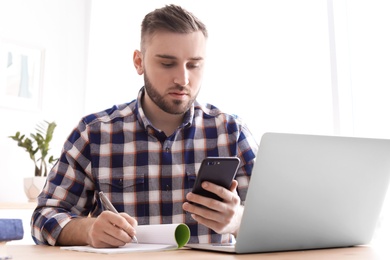 Photo of Young man working with mobile phone and laptop at desk. Home office