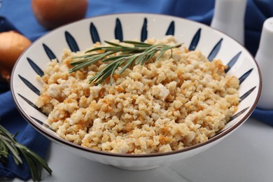 Photo of Fried ground meat in bowl and rosemary on white tiled table, closeup