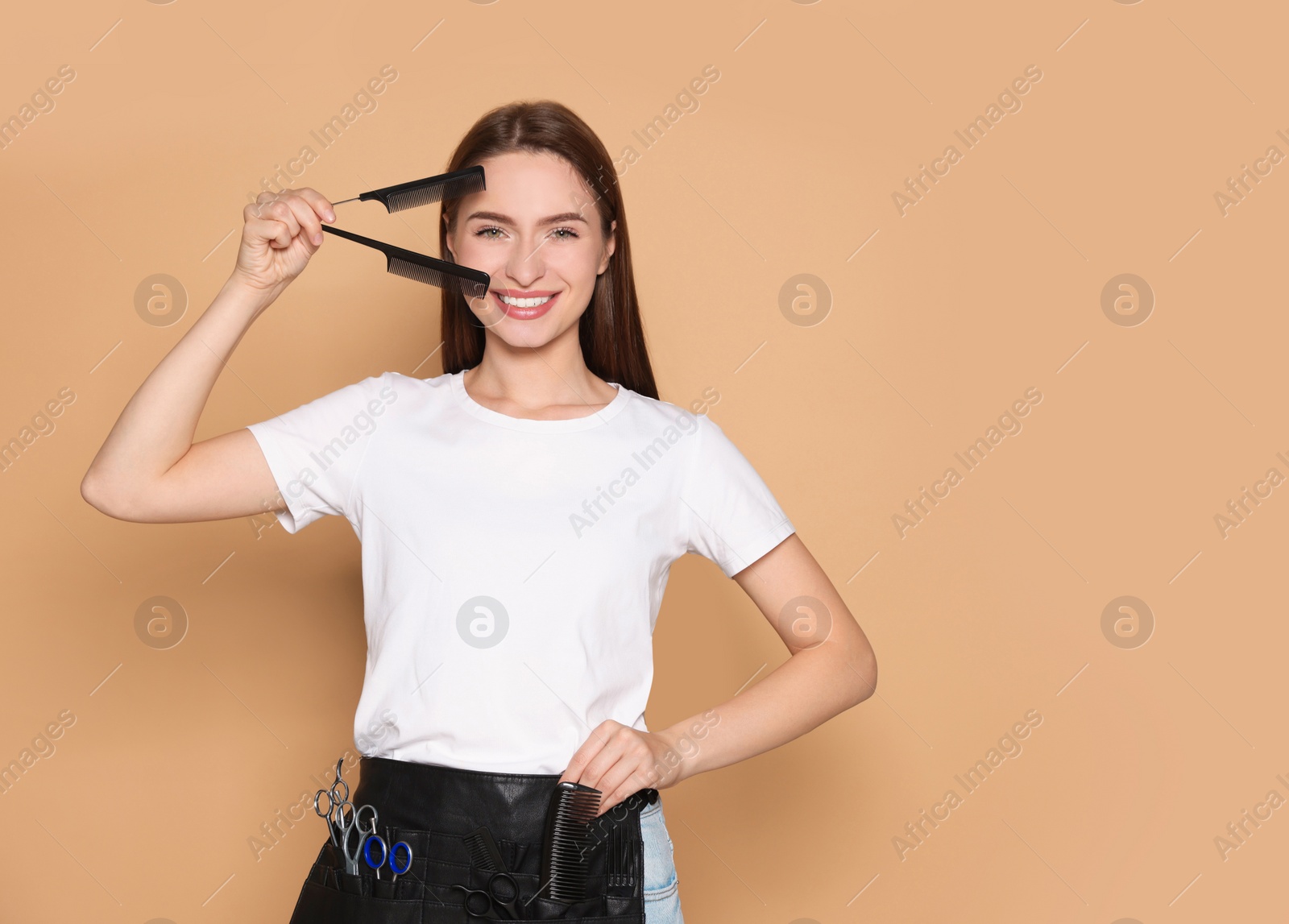 Photo of Portrait of happy hairdresser with combs on beige background. Space for text