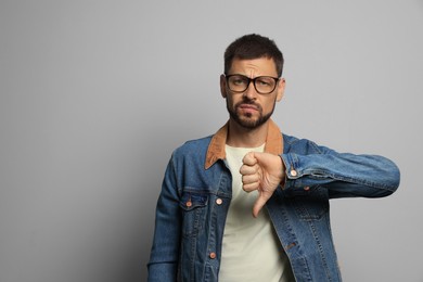 Man showing thumb down on grey background, space for text