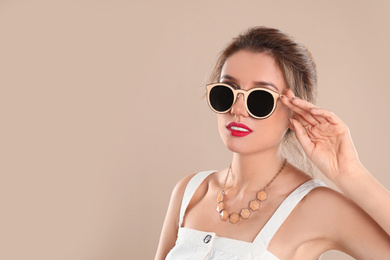 Photo of Young woman wearing stylish sunglasses on beige background. Space for text