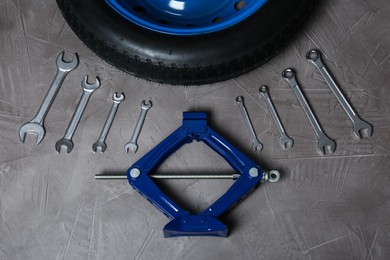 Photo of Car wheel, scissor jack and wrench set on grey surface, flat lay