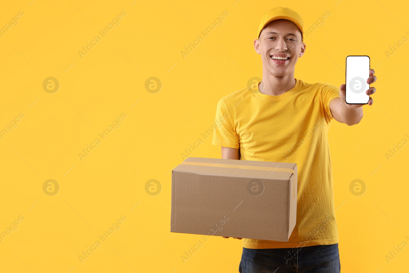 Photo of Happy courier with parcel and smartphone on orange background. Space for text