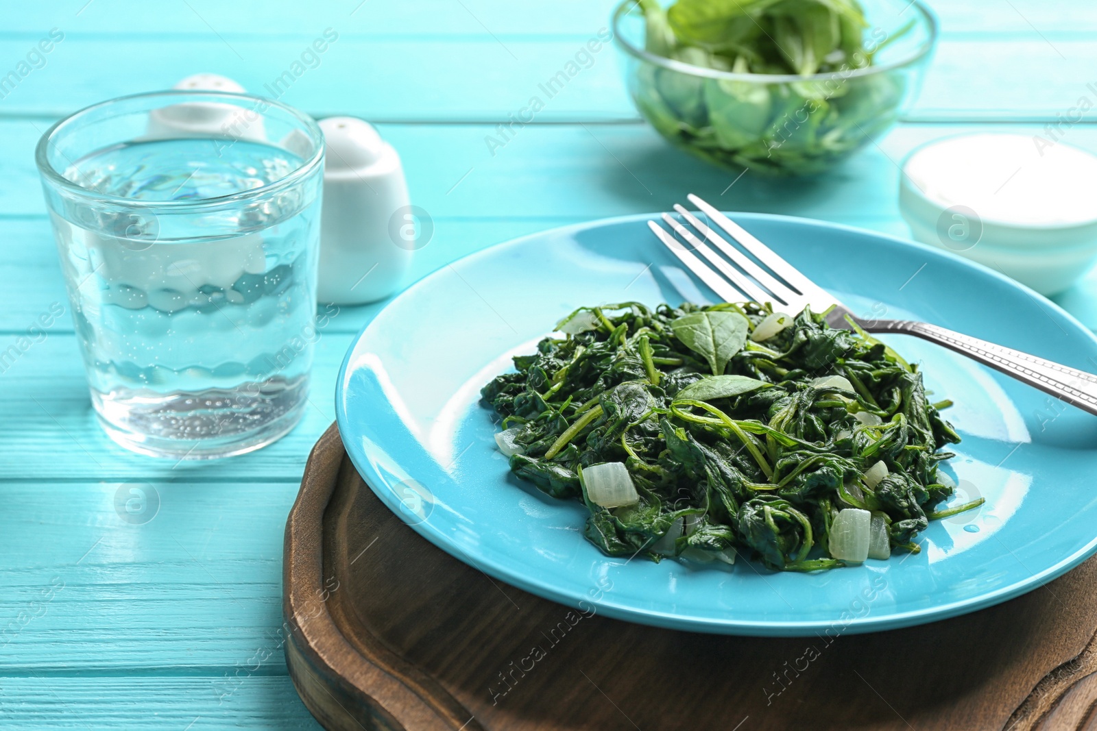 Photo of Tasty cooked spinach served on light blue wooden table. Healthy food