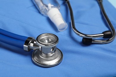 Photo of Stethoscope and antiseptic on light blue medical uniform, closeup