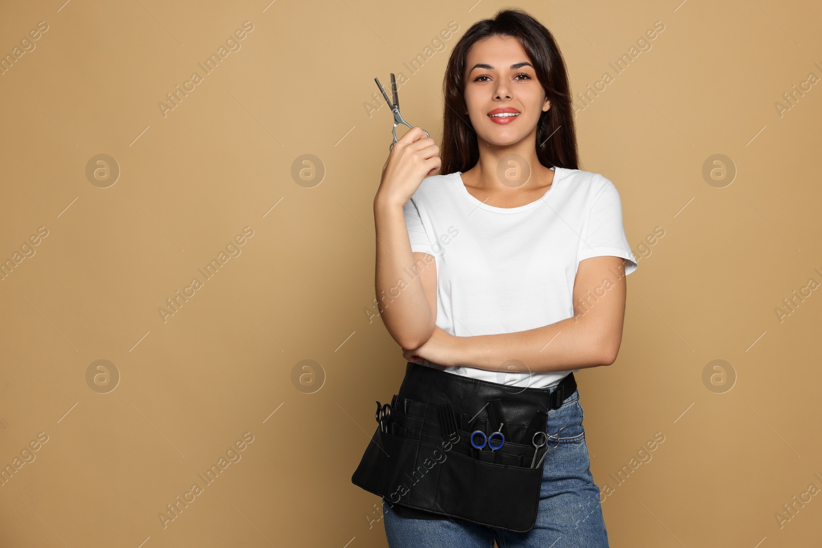 Photo of Portrait of happy hairdresser with professional scissors on pale orange background. Space for text