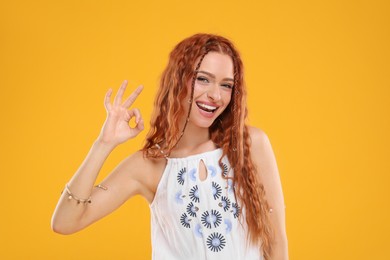 Photo of Beautiful young hippie woman showing OK gesture on orange background