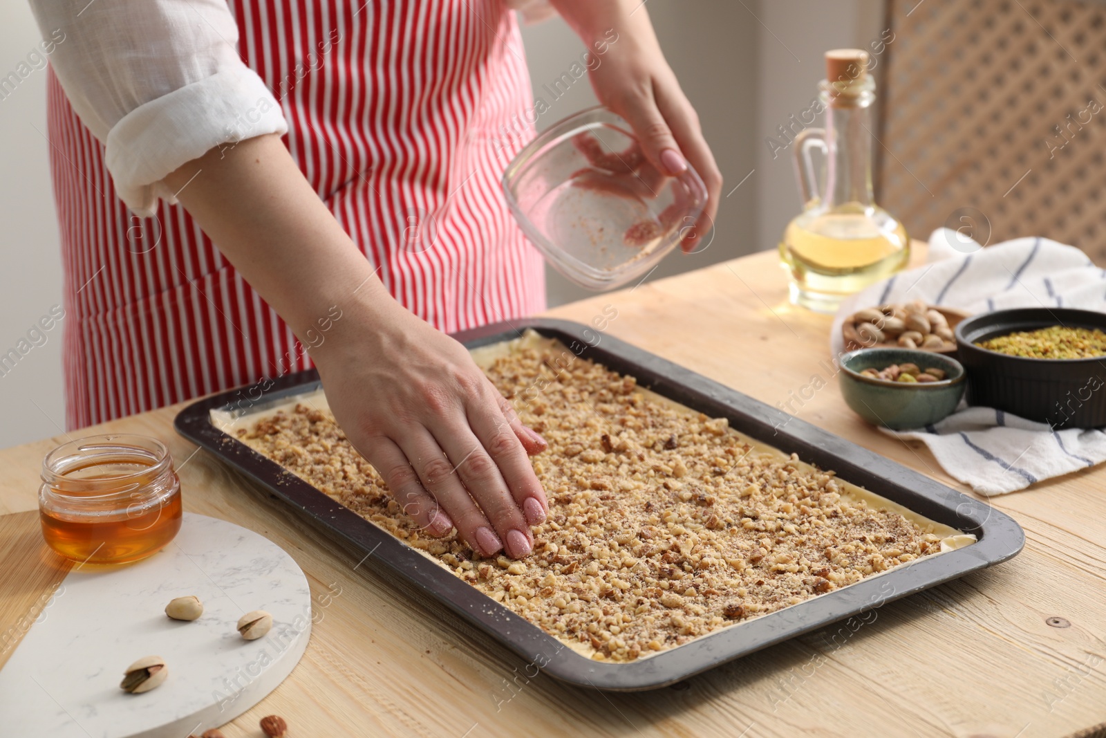 Photo of Making delicious baklava. Woman adding chopped nuts to dough at wooden table, closeup