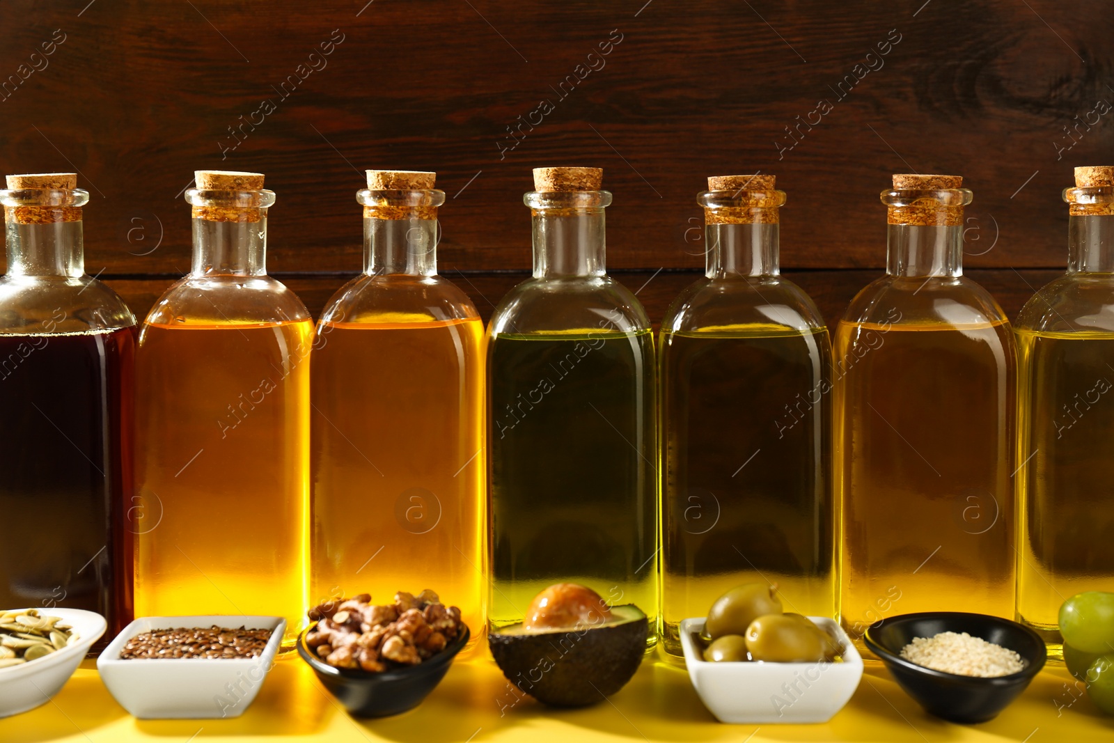 Photo of Vegetable fats. Different oils in glass bottles and ingredients on yellow table, closeup