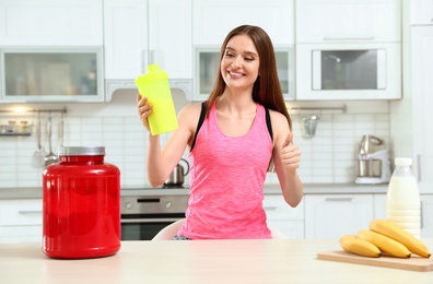 Young woman with bottle of protein shake in kitchen
