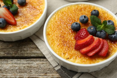 Delicious creme brulee with berries and mint in bowls on wooden table, closeup