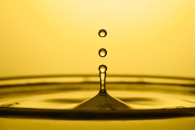 Image of Splash of golden oily liquid with drops on yellow background, closeup
