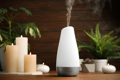 Photo of Composition with modern aroma humidifier on wooden table against brown background, space for text