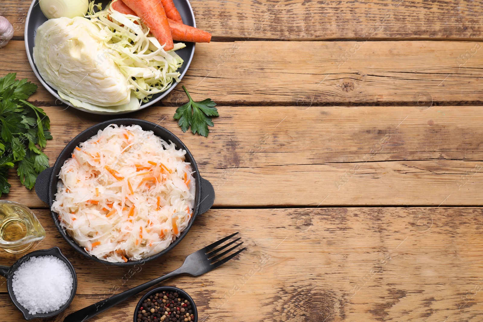 Photo of Bowl of tasty sauerkraut and ingredients on wooden table, flat lay. Space for text