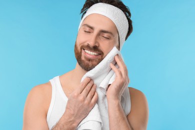 Photo of Washing face. Man with headband and towel on light blue background