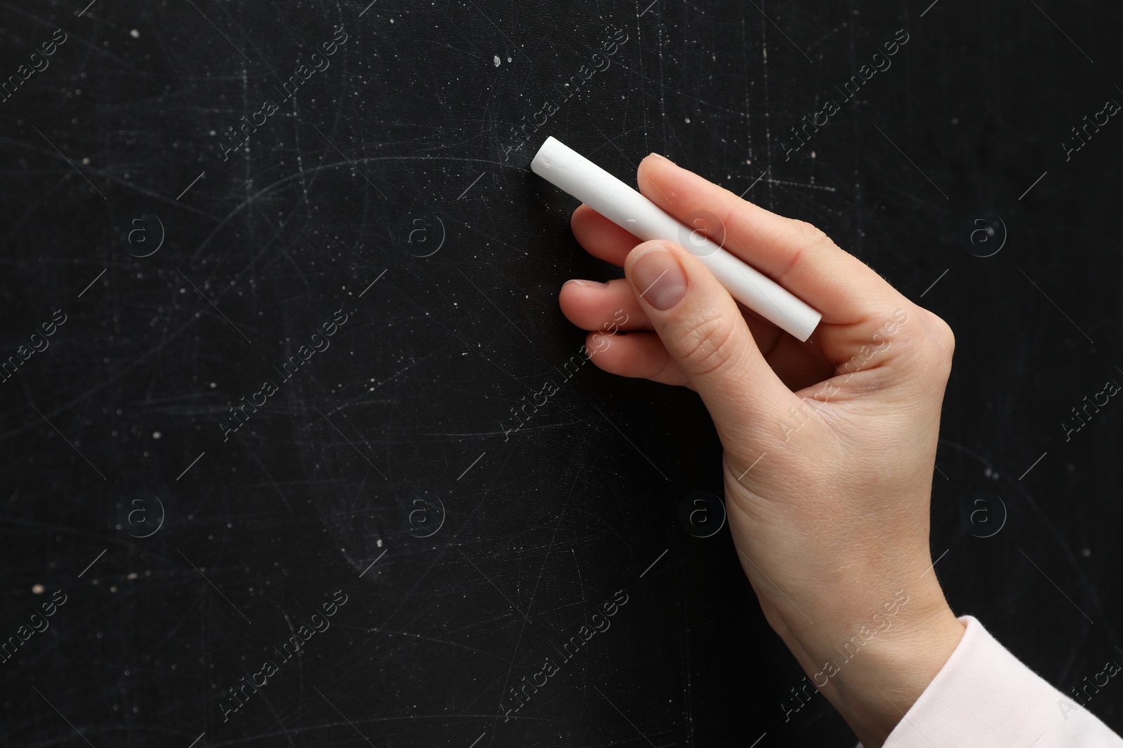 Photo of Teacher writing with chalk on black chalkboard, closeup. Space for text