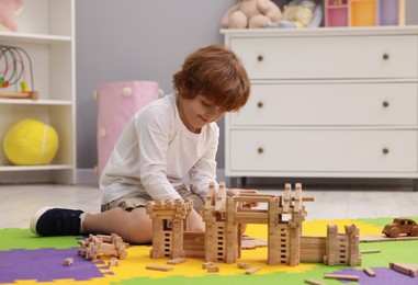 Little boy playing with wooden construction set on puzzle mat in room. Child's toy