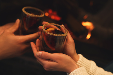 Couple with mulled wine near fireplace indoors, closeup. Winter vacation