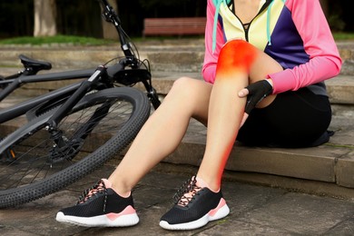 Woman with injured knee on steps near bicycle outdoors, closeup