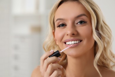 Photo of Beautiful makeup. Smiling woman applying liquid lipstick indoors, closeup. space for text