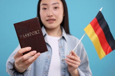 Photo of Immigration to Germany. Happy woman with passport and flag on light blue background, selective focus