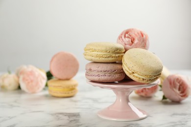 Photo of Delicious macarons and flowers on white marble table