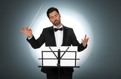 Professional conductor with baton and note stand on grey background