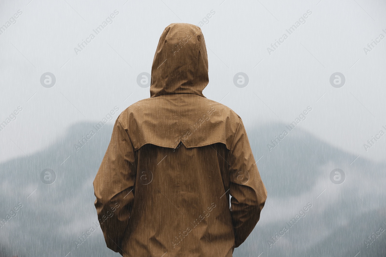 Photo of Woman in raincoat enjoying mountain landscape under rain, back view