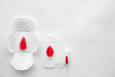 Photo of Flat lay composition with feminine hygiene items and red feathers on light background. Gynecological care