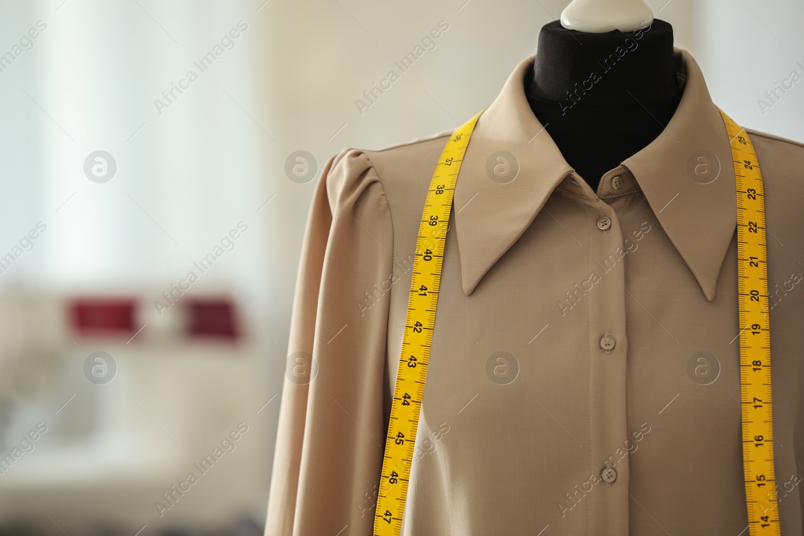 Photo of Mannequin with shirt and measuring tape in tailor shop, space for text