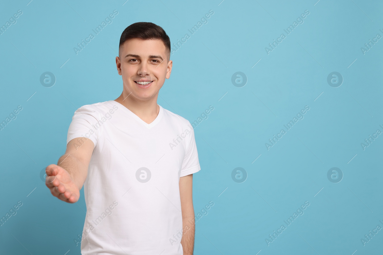 Photo of Handsome man inviting to come in against light blue background. Space for text