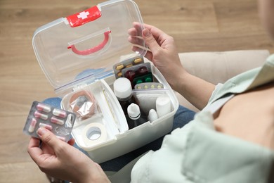 Woman putting pills into first aid kit indoors, closeup