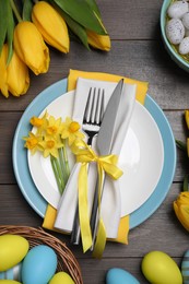 Photo of Festive table setting with flowers and painted eggs on wooden background, flat lay. Easter celebration