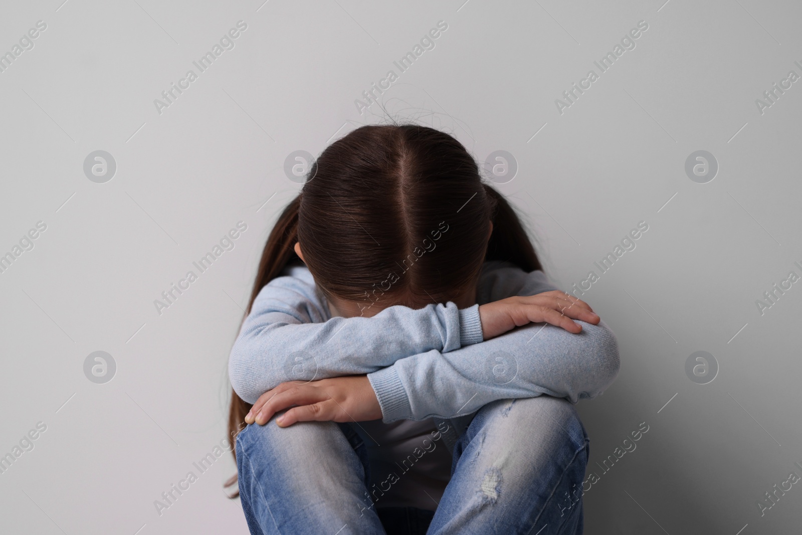 Photo of Child abuse. Upset little girl near light grey wall