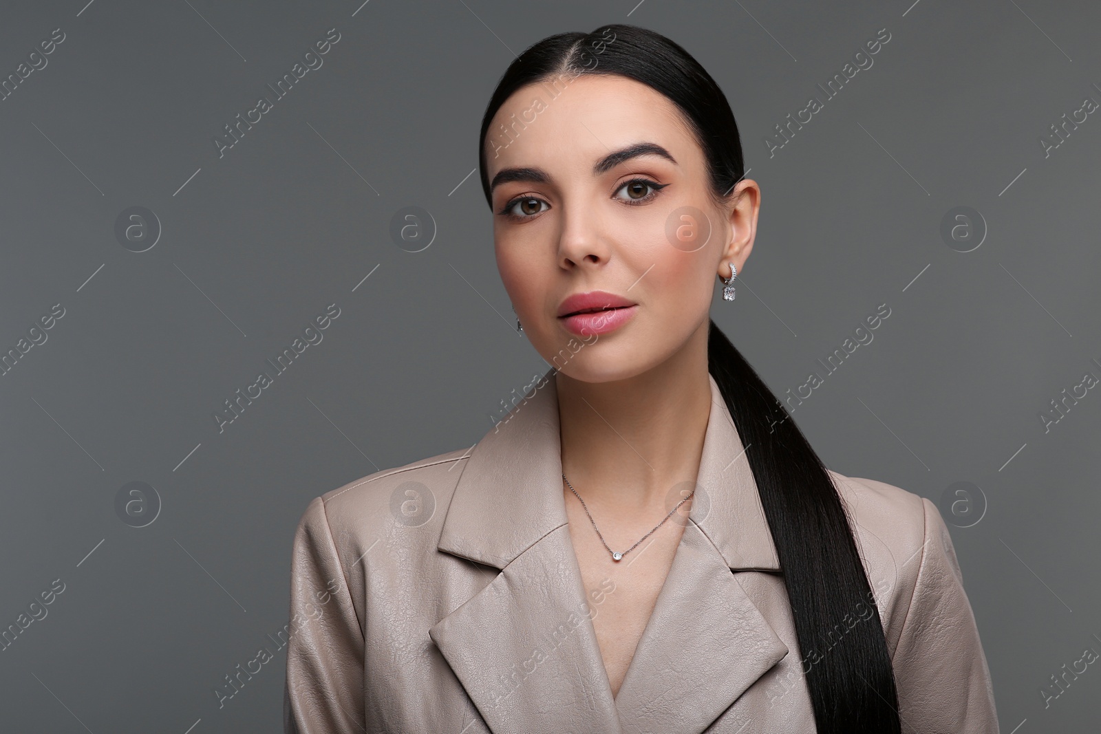 Photo of Beautiful young woman with elegant jewelry on dark grey background