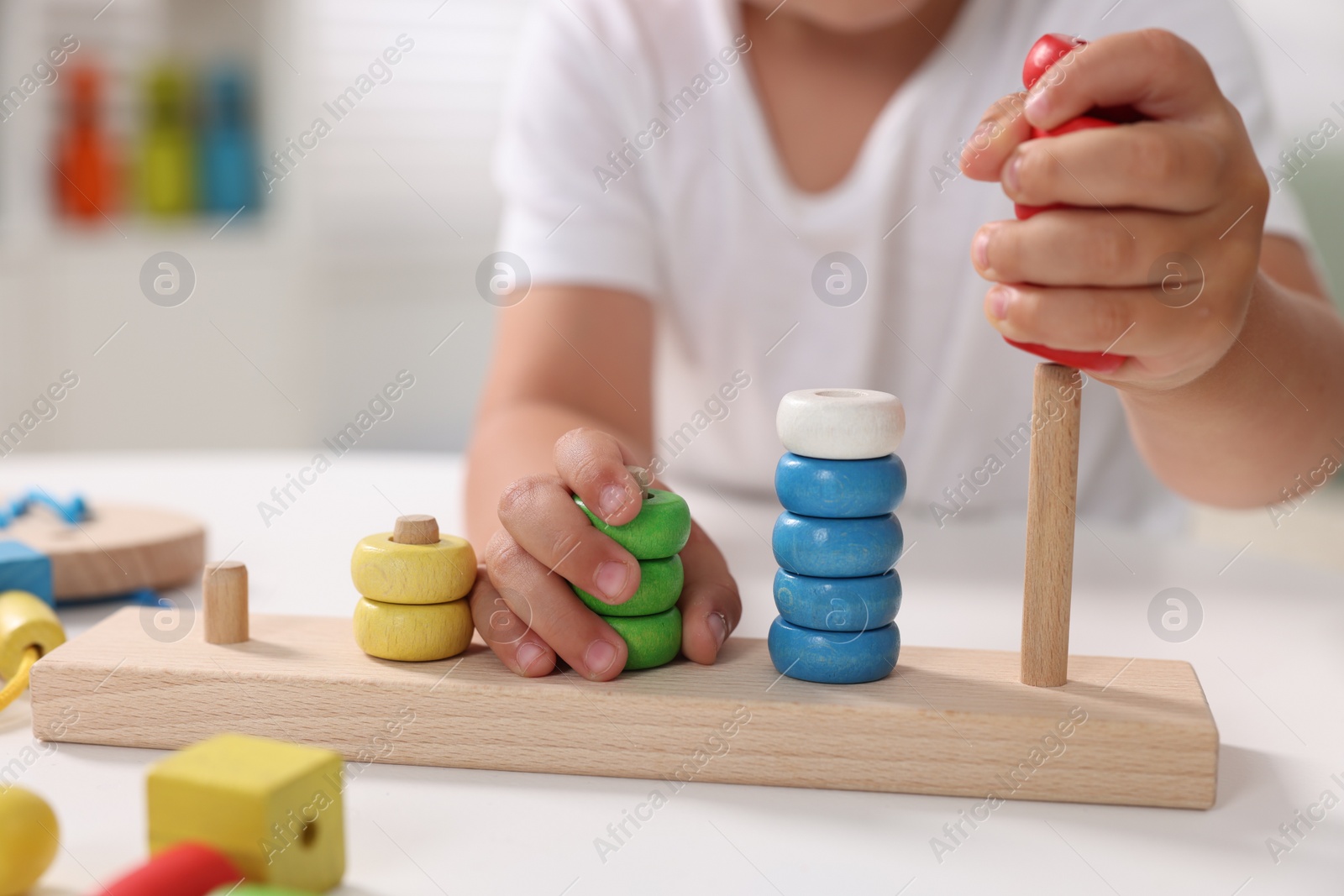 Photo of Motor skills development. Little boy playing with stacking and counting game at table indoors, closeup