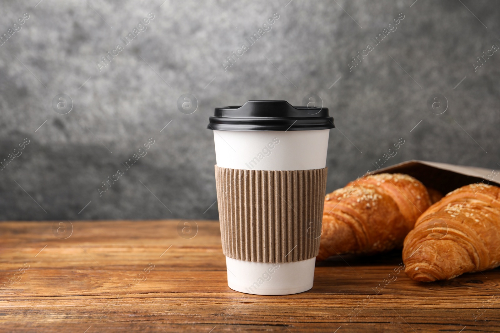 Photo of Coffee to go. Paper cup with tasty drink and pastry on wooden table. Space for text