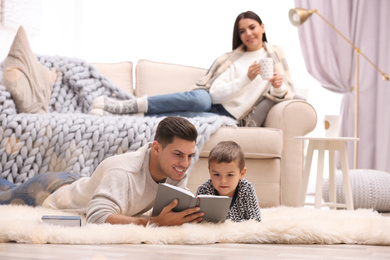 Father and his son reading books while mother resting on sofa at home. Winter vacation