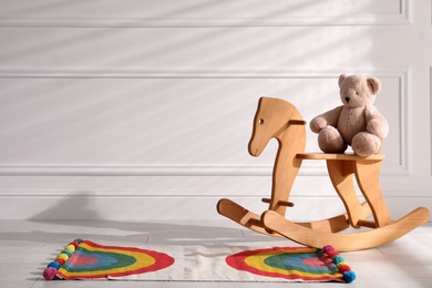 Cute toy bear on rocking horse in baby room, space for text. Interior design