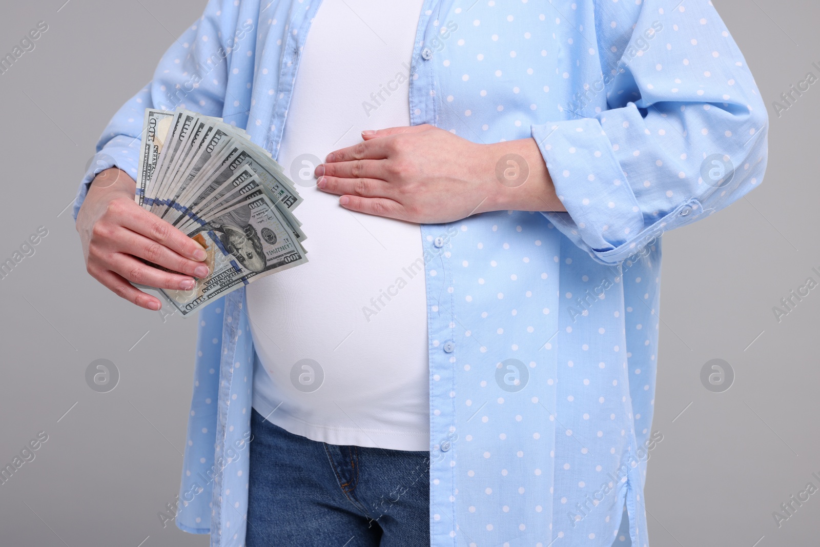 Photo of Surrogate mother. Pregnant woman with dollar banknotes on light grey background, closeup