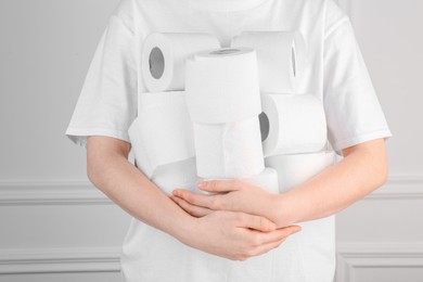 Photo of Woman with many toilet paper rolls near white wall, closeup